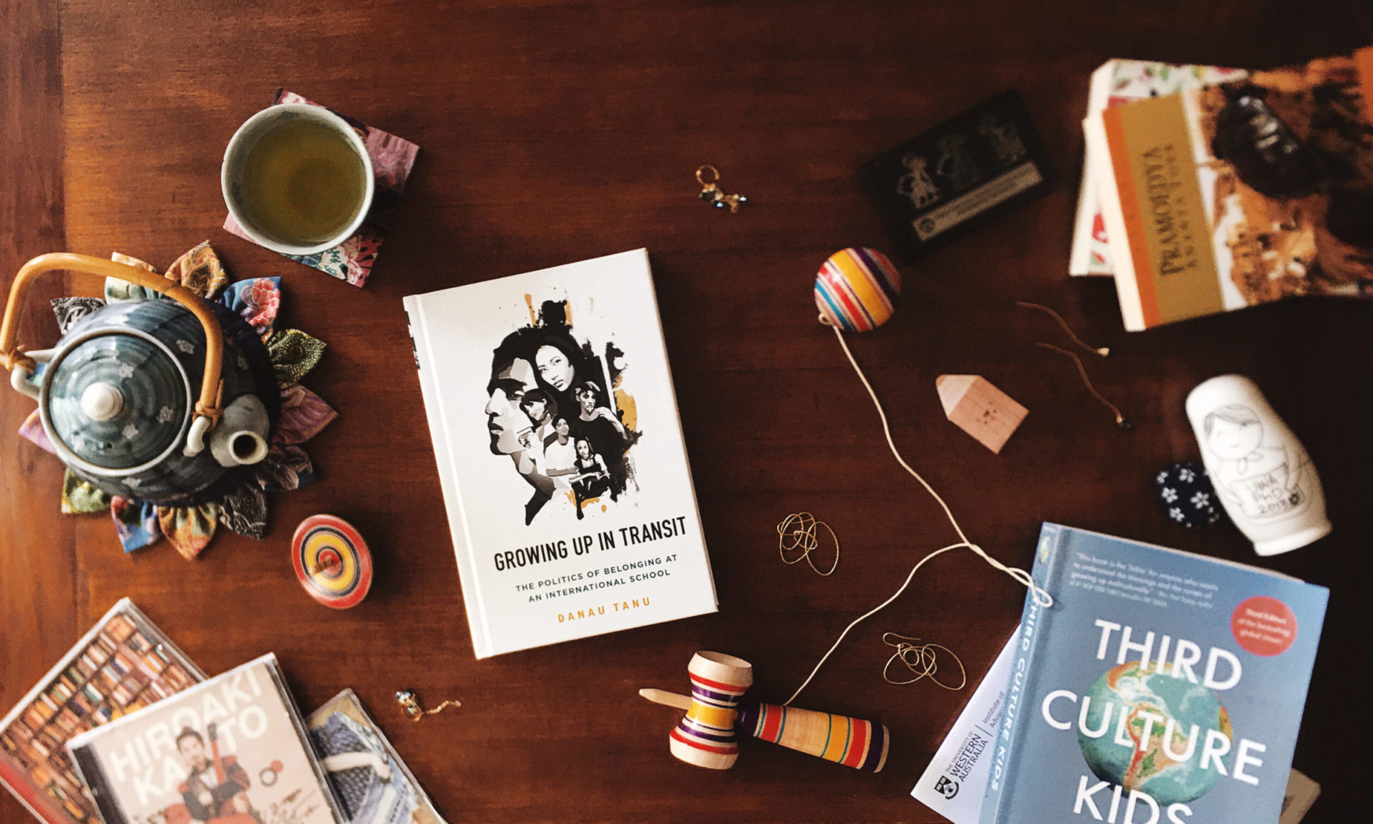 Photo of books, teapots and trinkets on a table, including Growing Up in Transit and Third Culture Kids, arranged in a flatlay