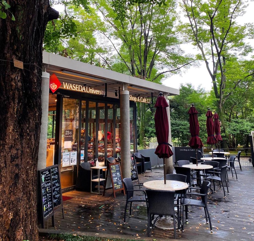 Photo of the Waseda University Uni Shop & Cafe 125. Outdoor seating in the front, trees in the background.