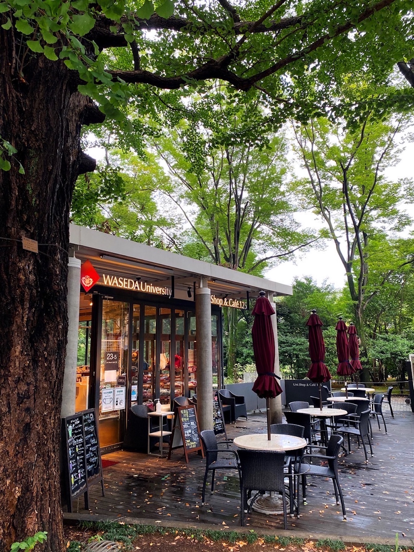 Photo of the Waseda University Uni Shop & Cafe 125. Outdoor seating in the front, trees in the background.